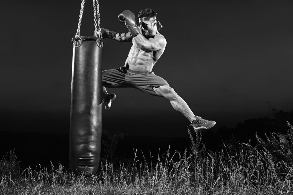black-white-shot-male-kick-boxer-jumping-kicking-heavy-punching-bag-training-outdoors-copyspace-professional-skilled-motivation-sports-competitive-preparing-achievement-fighting-toned